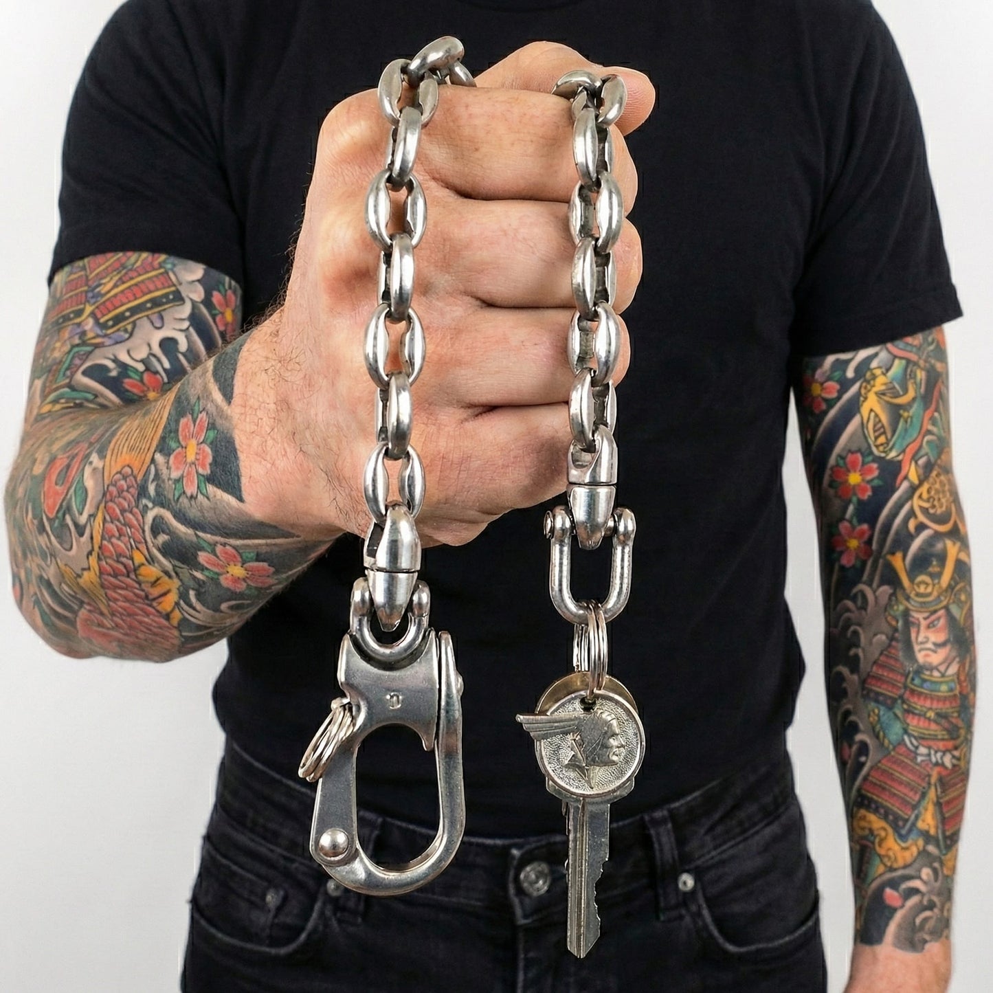 Massive Edelstahl Wallet Chain als Schlüsselkette mit großem Karabiner und Schlüsselring, gehalten von tätowiertem Mann im Biker- und Rocker-Style.