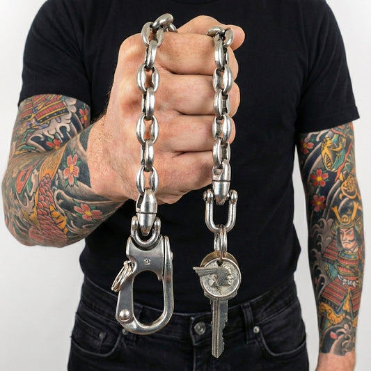 Massive Edelstahl Wallet Chain als Schlüsselkette mit großem Karabiner und Schlüsselring, gehalten von tätowiertem Mann im Biker- und Rocker-Style.