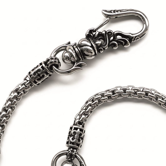 Detailaufnahme einer geflochtenen Edelstahl-Hosenkette mit verziertem Ornamenthaken, leicht geschwärztem Finish und beweglicher Kettenstruktur.